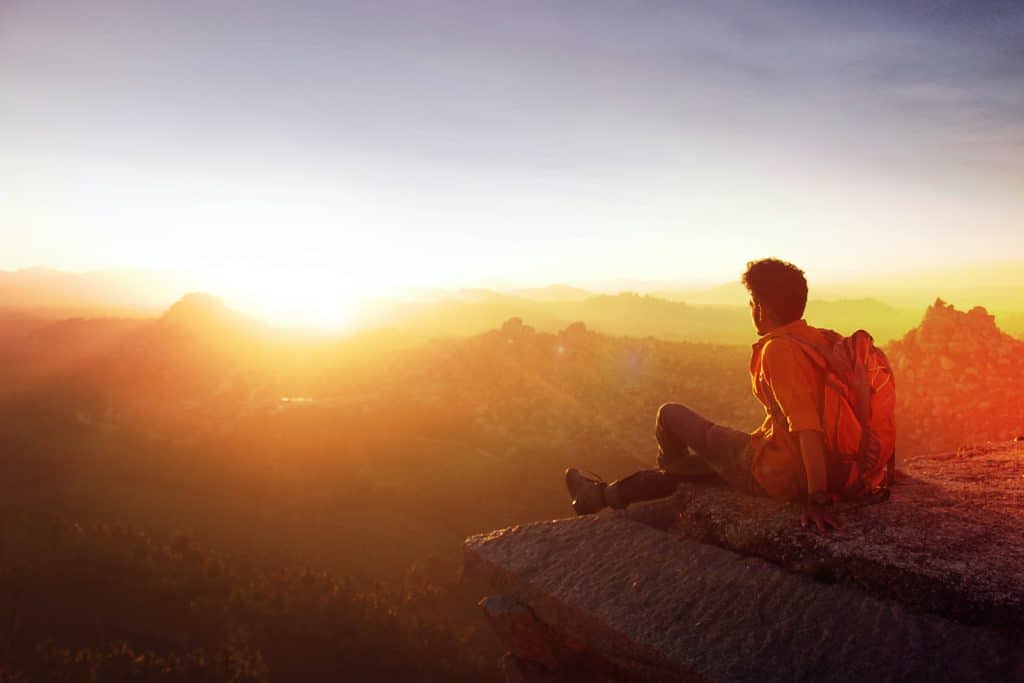 man sitting on edge facing sunset 915972